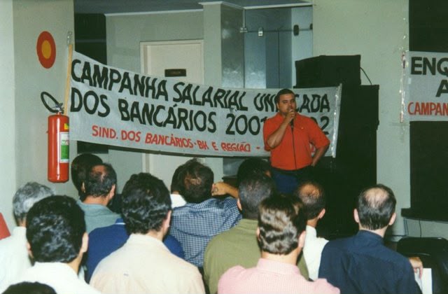 Dirigente sindical de camisa vermelha fala em reunião da campanha salarial dos bancários.