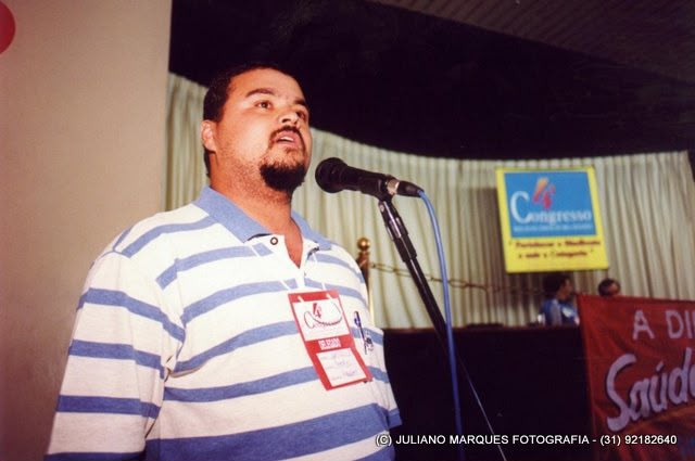 Dirigente com camisa listrada e credencial fala ao microfone em encontro sindical.