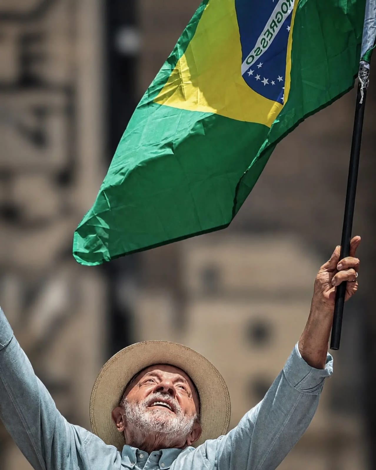 Lula ergue os braços e segura uma bandeira brasileira.